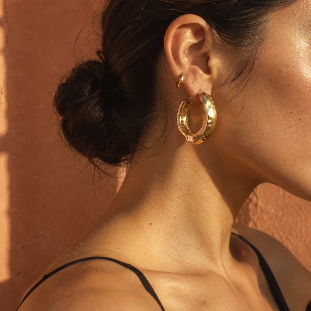 Chunky hammered gold hoop earring in warm sunlight against terracotta