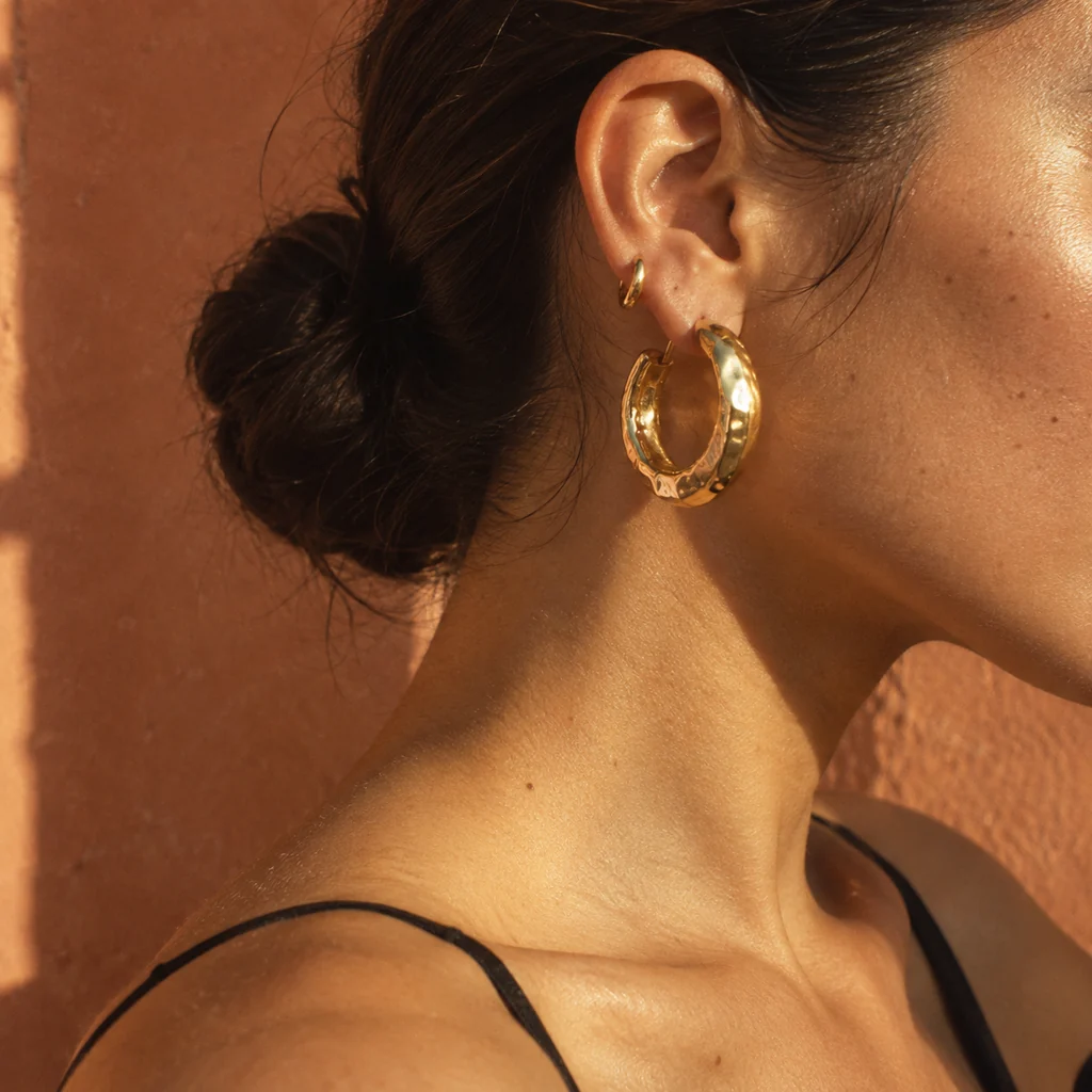 Chunky hammered gold hoop earring in warm sunlight against terracotta