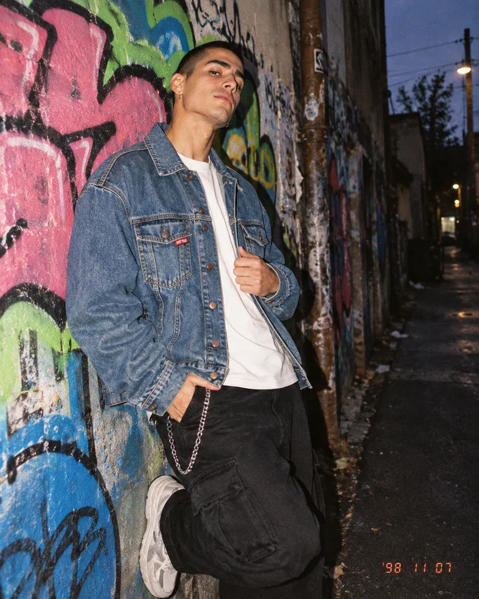 Man in a stonewashed denim jacket against a graffiti wall in flash light