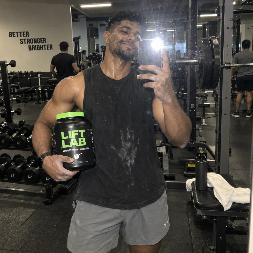 Post-workout gym mirror selfie holding a black and lime protein tub